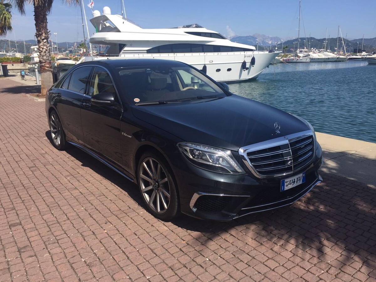 Black Mercedes E-Class luxury sedan parked in front of a private yacht at a marina, for executive port transfers and business class service in Tuscany