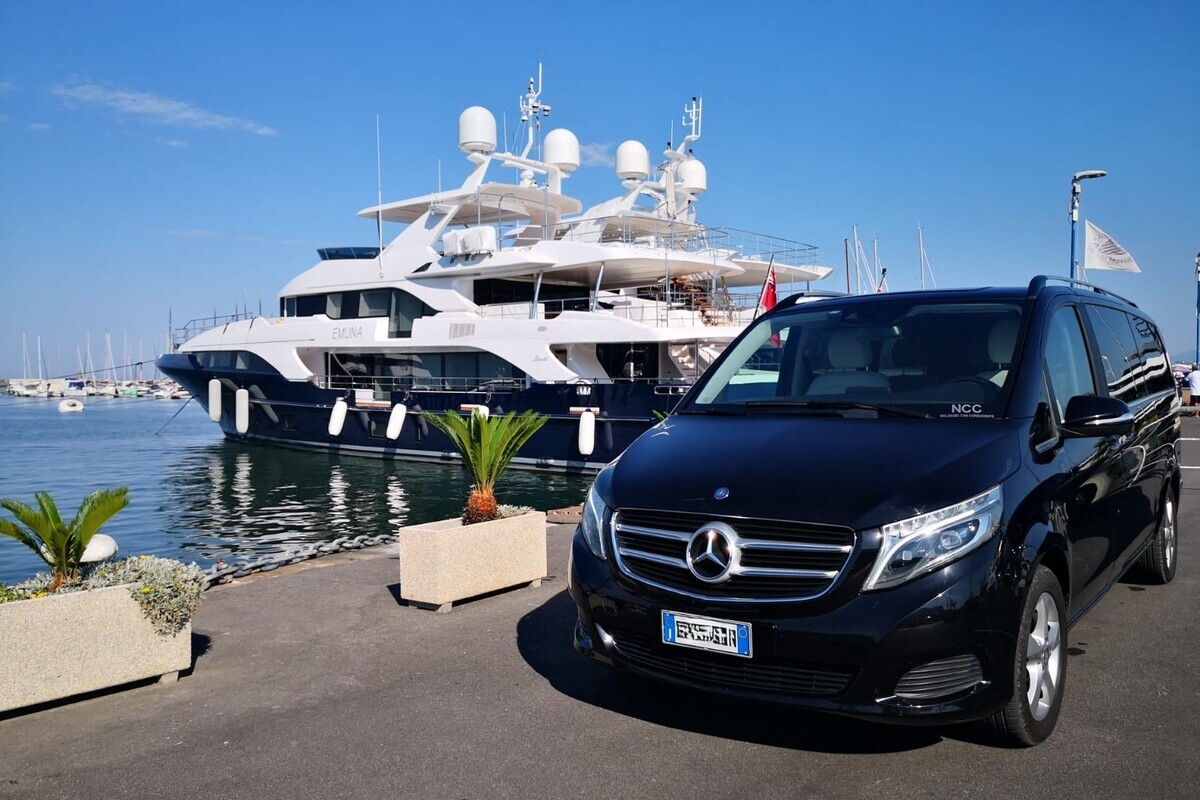 White Mercedes V-Class luxury van parked on Viareggio marina waterfront with a yacht in the background, Florence Pisa Taxi service