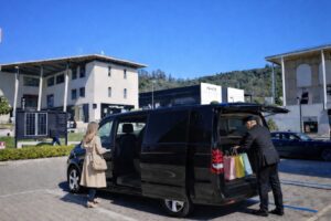 Private chauffeur assisting a woman boarding a Mercedes van with shopping bags at The Mall Florence.