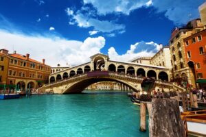 View of the Rialto Bridge over the Grand Canal in Venice, with gondolas and historic buildings at sunset.