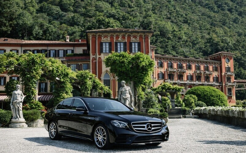 Luxury black executive sedan parked in front of Villa d'Este on Lake Como, elegant hotel entrance with Italian lake view
